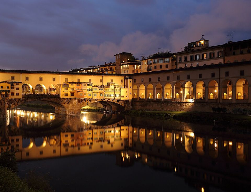 Il Ponte Vecchio al crepuscolo, di scorcio, accanto al porticato illuminato del lungarno