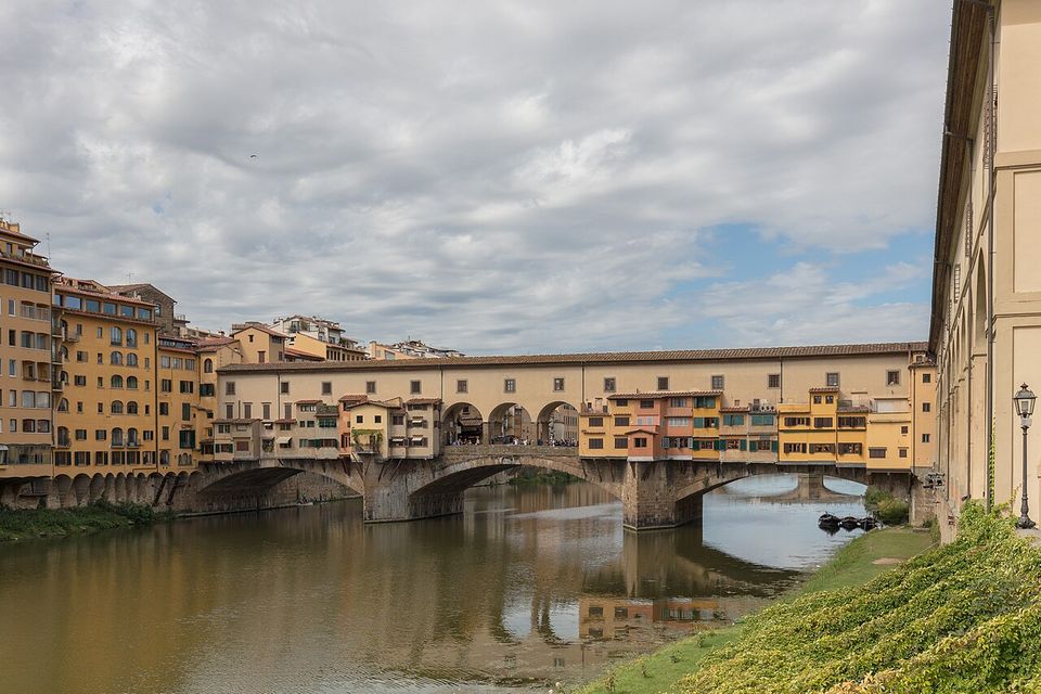 Il Ponte Vecchio di scorcio dal lungarno sotto un cielo nuvoloso, con le botteghe riflesse nell'Arno
